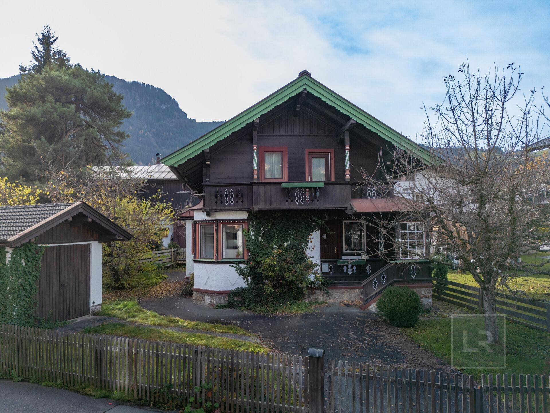 Charmantes alpines Haus mit traditioneller Holzfassade, Balkon und umzäuntem Vorgarten.