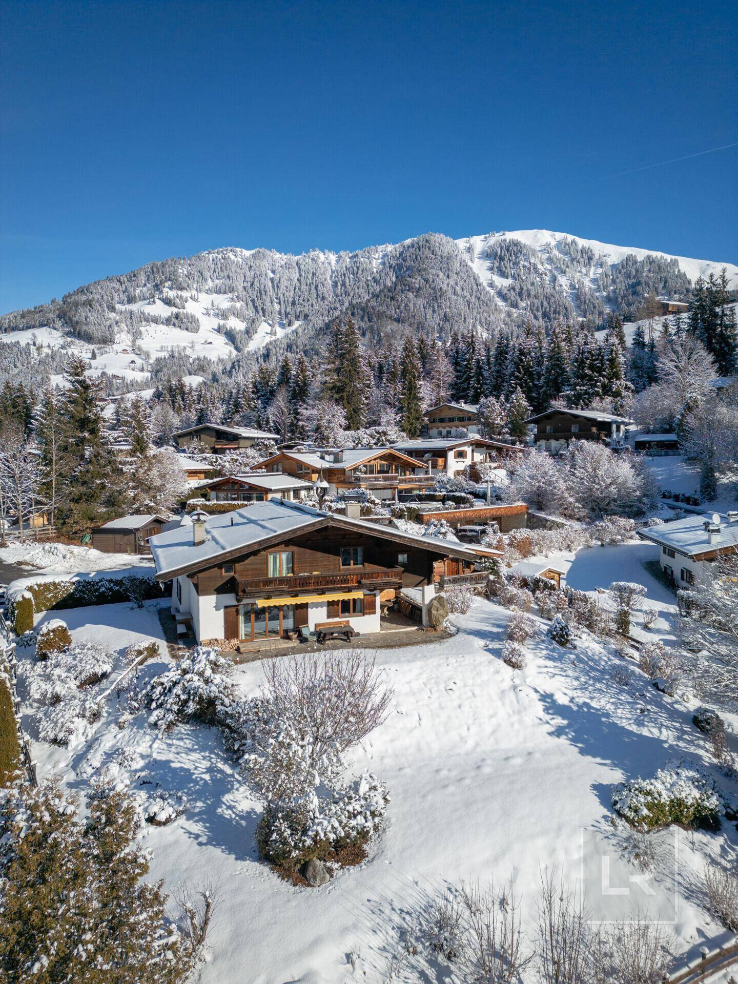Panoramablick auf eine Ansammlung von Chalets in einer verschneiten Berglandschaft unter strahlendem Sonnenschein.