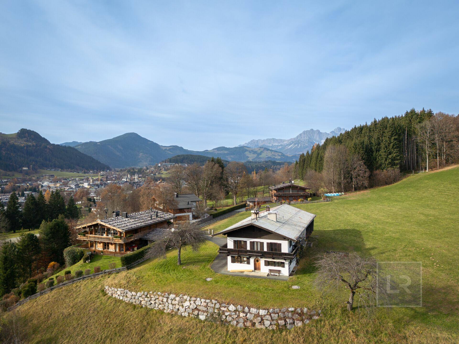 Luftaufnahme des Anwesens mit umliegenden Häusern, Dorf und majestätischer Bergkulisse im Herbst.