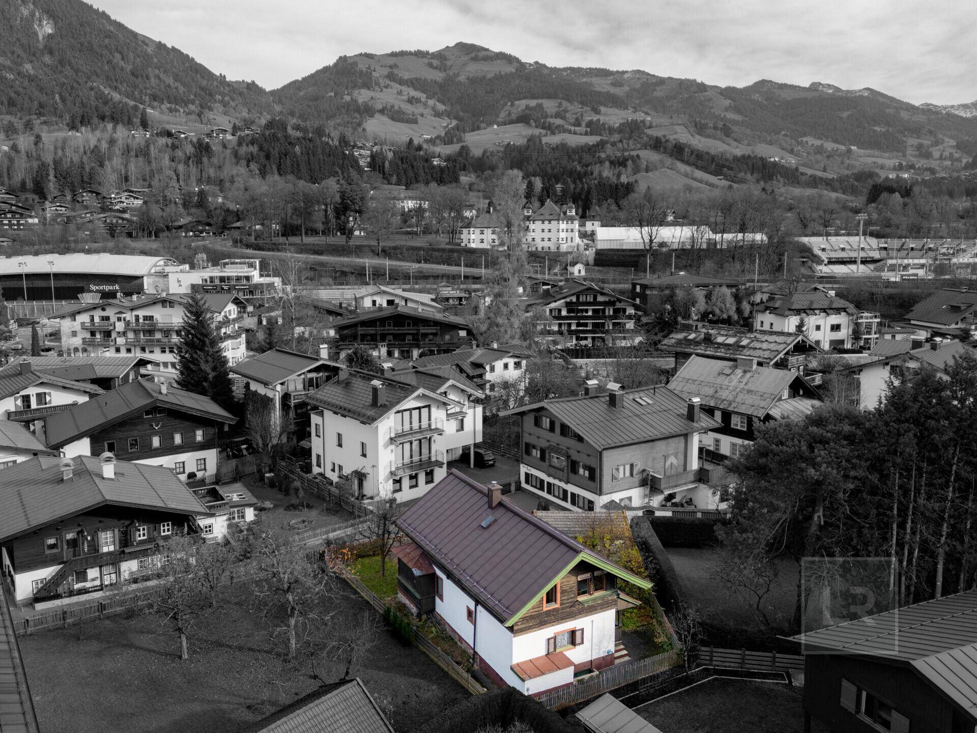 Vogelperspektive des Hauses in einer Siedlung, umgeben von Bergen, mit farblich hervorgehobenem Dach.