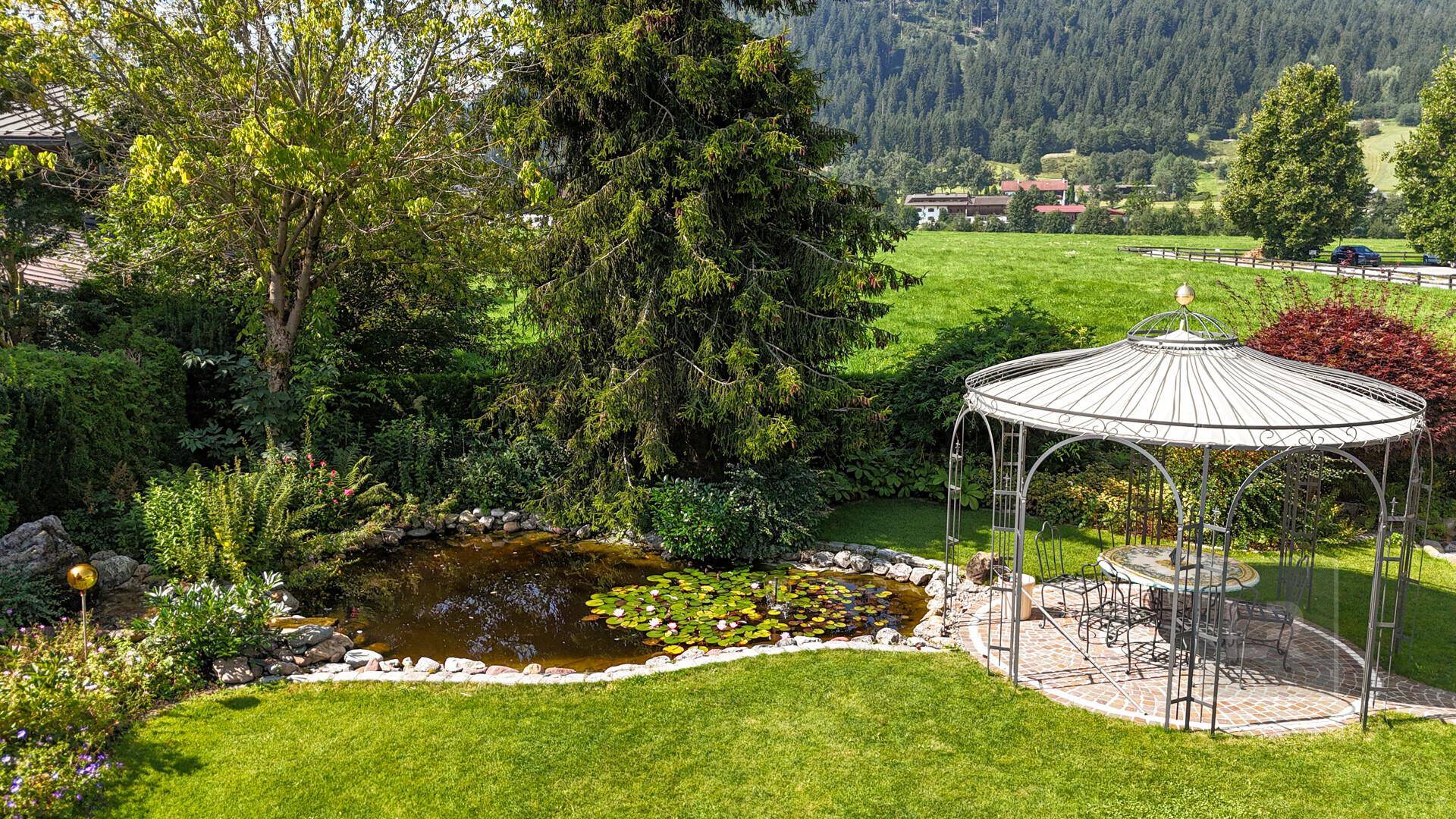 Idyllischer Gartenbereich mit Teich, Seerosen und einem charmanten Pavillon, umgeben von üppigem Grün.