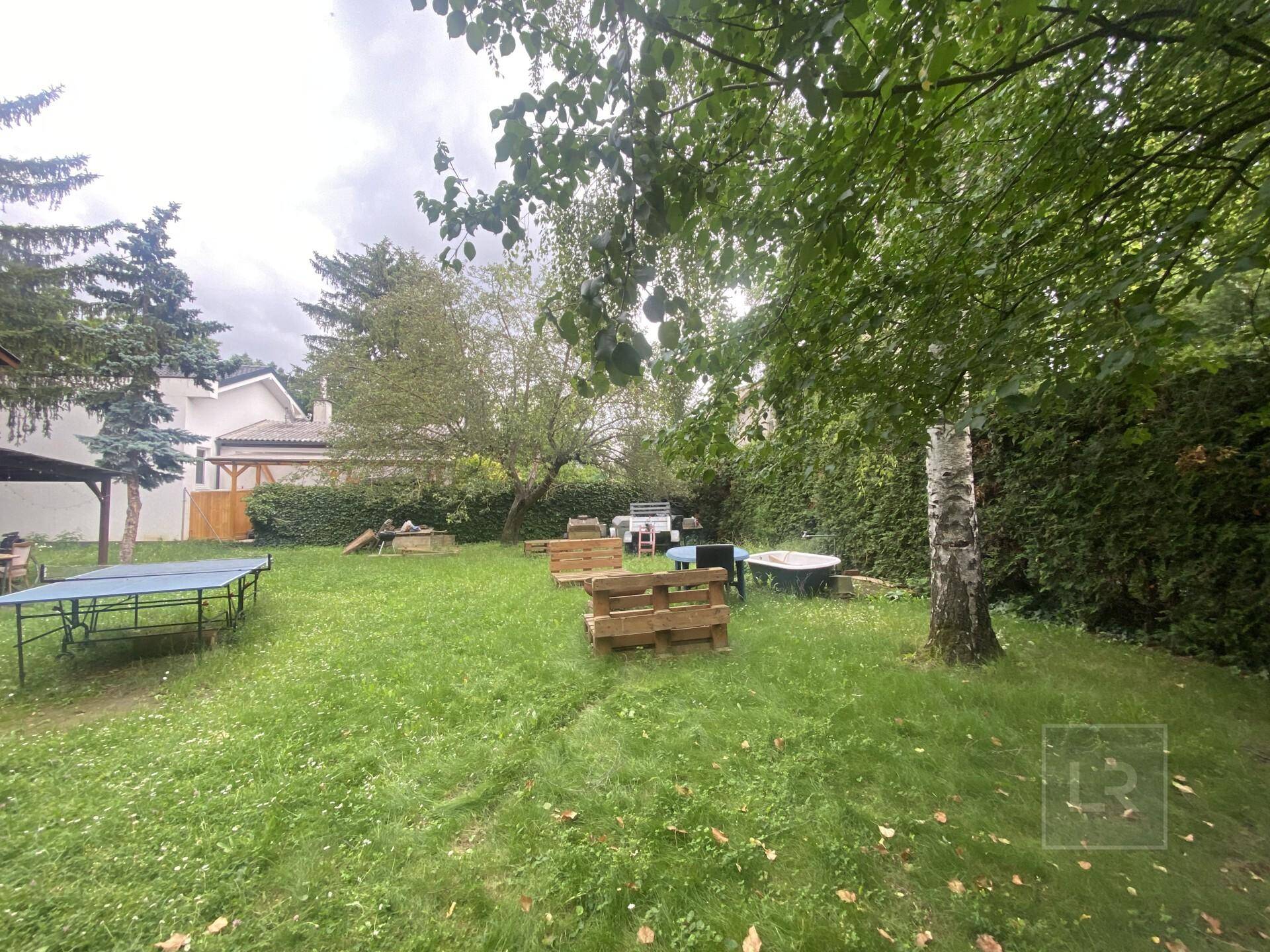 Weitläufiger Gartenbereich mit viel Grün, Bäumen und einer provisorischen Sitzecke.