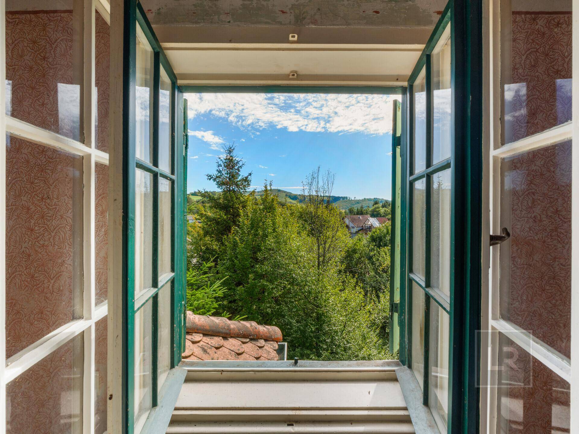 Malerischer Ausblick aus einem geöffneten Fenster auf grüne Hügel und die umliegende Landschaft.