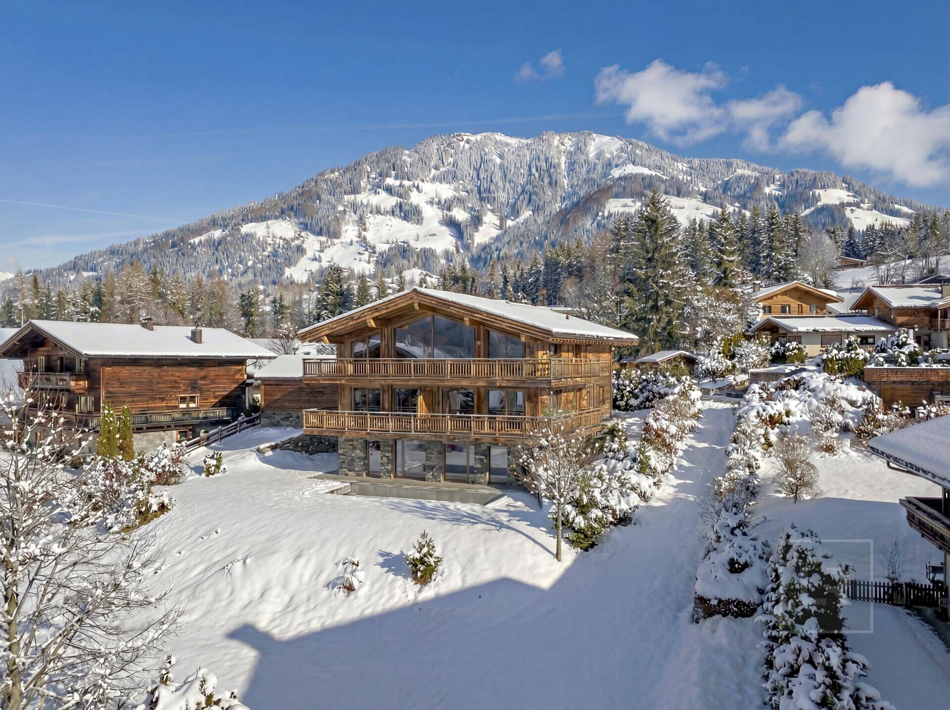 Nahaufnahme eines modernen Holzchalets mit großen Glasfronten und Balkonen vor verschneiten Bergen.