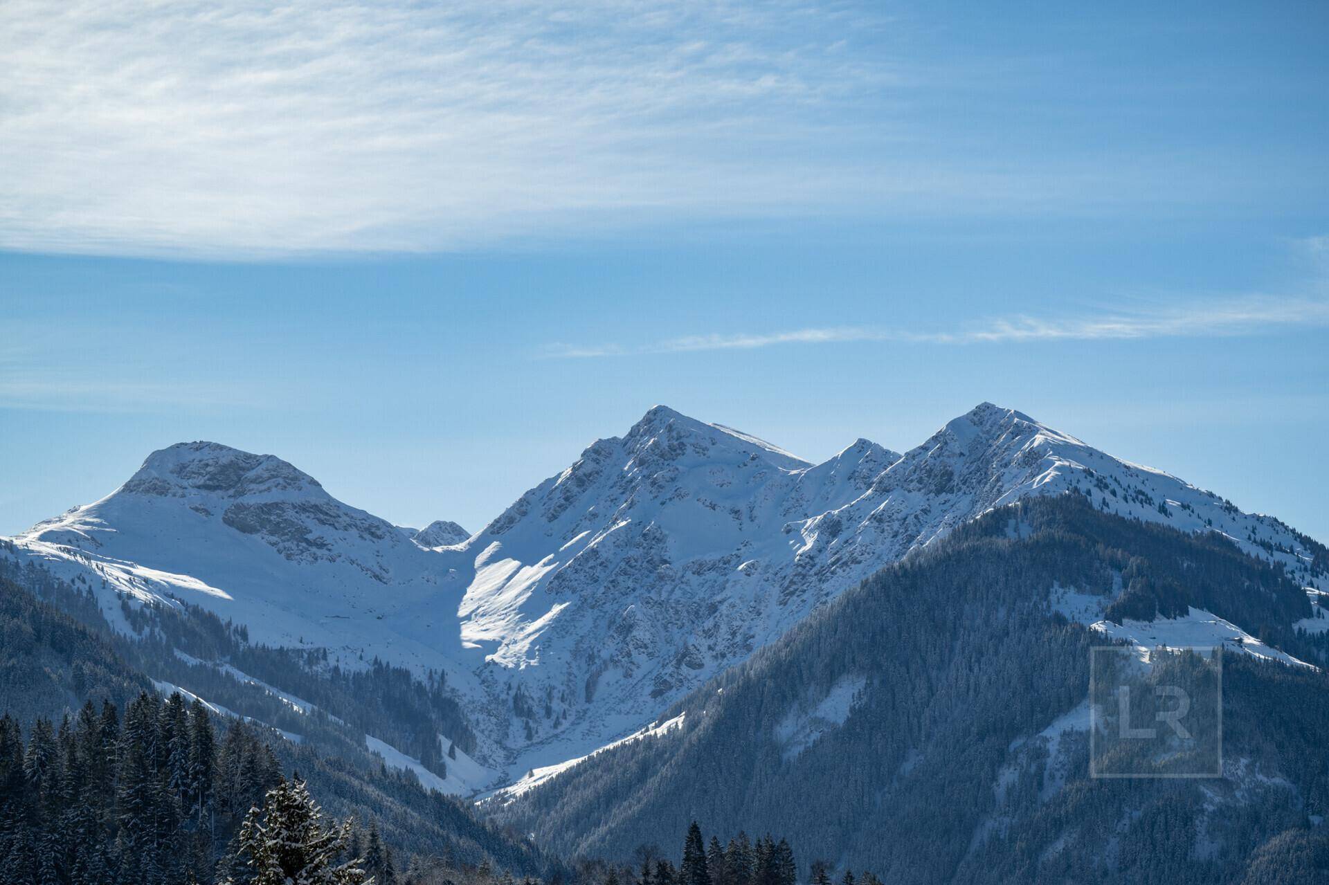 Majestätische, schneebedeckte Berggipfel unter einem weiten, blauen Himmel mit einigen Wolken.
