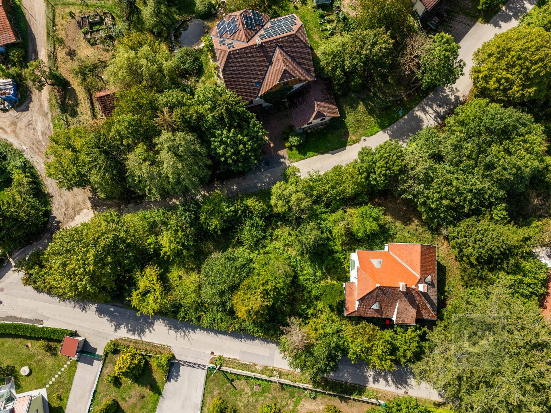 Weitläufige Luftaufnahme der Villa und ihrer grünen Umgebung mit weiteren Häusern und Straßen.