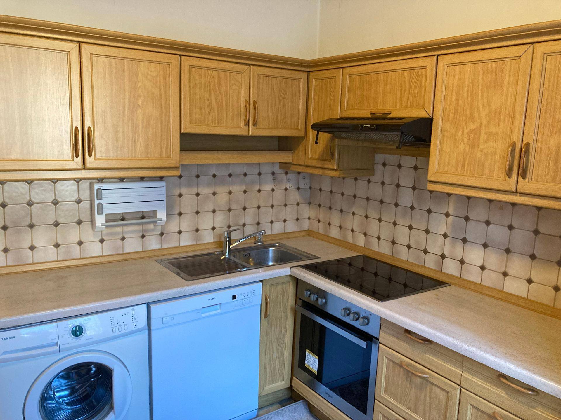 Küche mit Holzfronten, Induktionskochfeld, Backofen, Spülmaschine und Dunstabzugshaube.