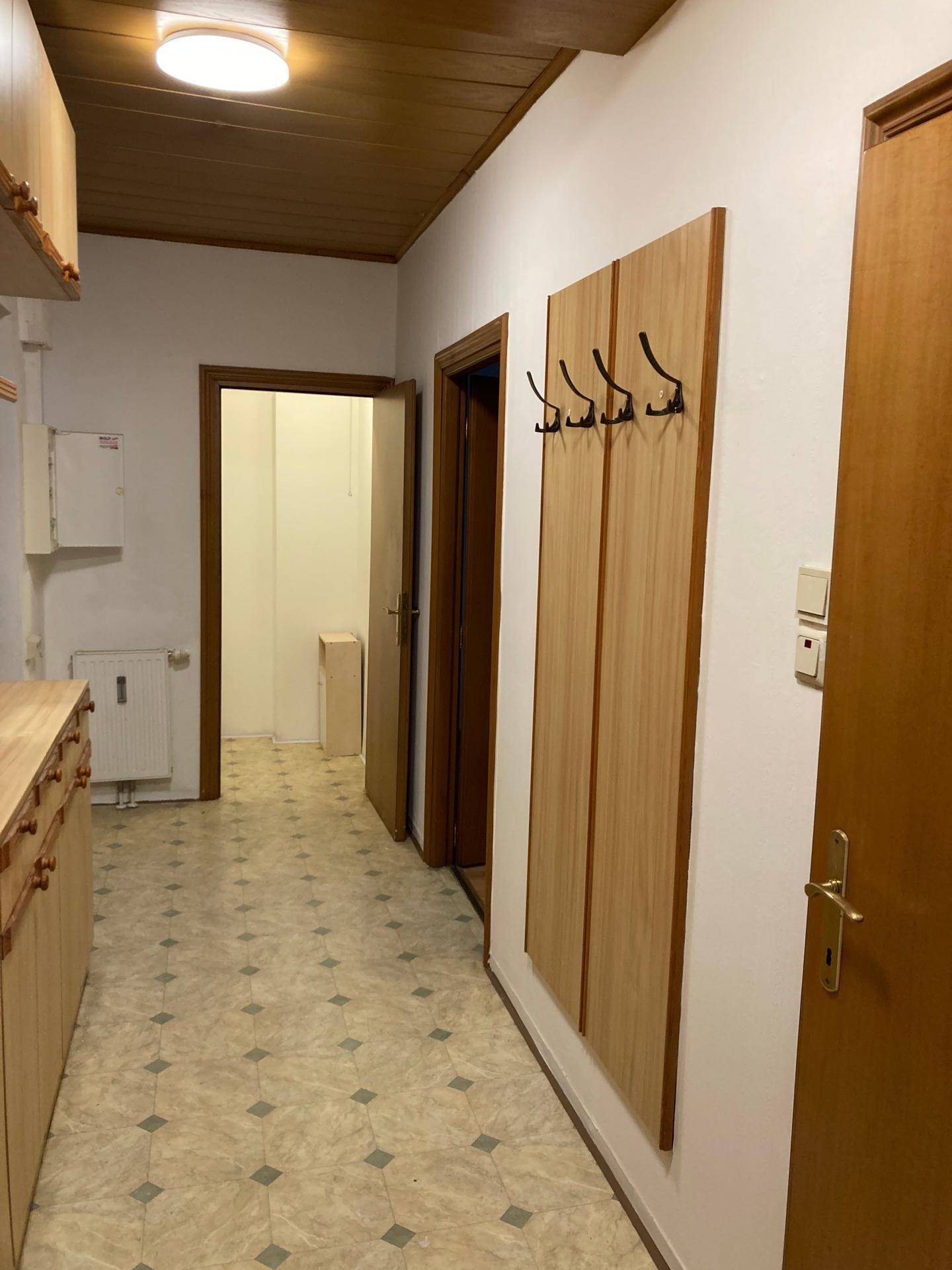 Flur mit Holzdecke, Linoleumboden und Garderobe, der zu weiteren Räumen führt.
