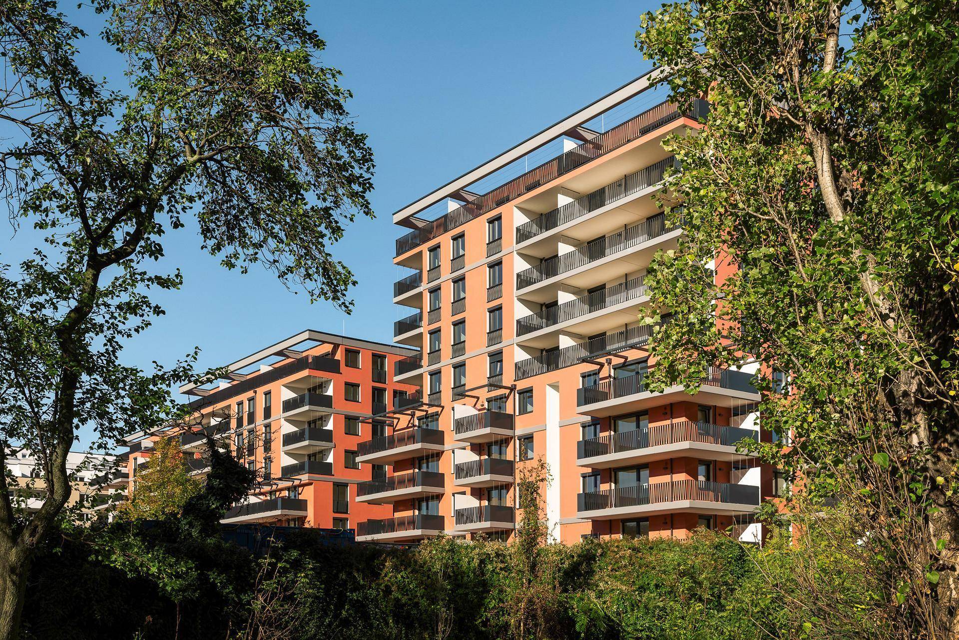 Moderne Apartmentgebäude mit zahlreichen Balkonen, umgeben von üppigem Grün und Bäumen.