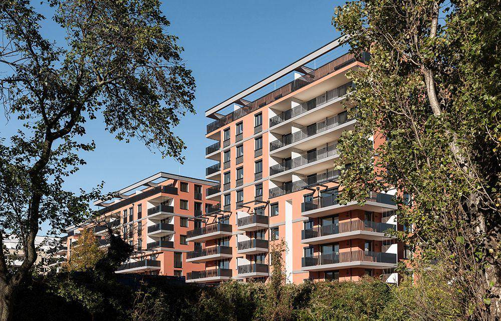 Modernes Wohngebäude mit orangefarbener Fassade und Balkonen, umgeben von üppigem Grün und Bäumen.