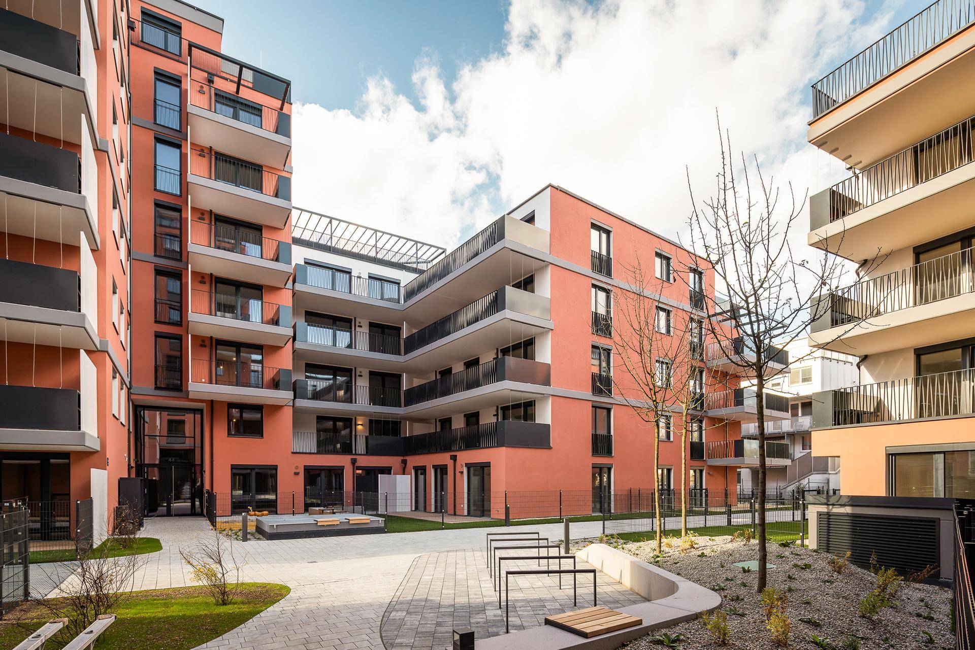 Moderne Wohngebäude mit orangefarbenen Fassaden und Balkonen um einen begrünten Innenhof.