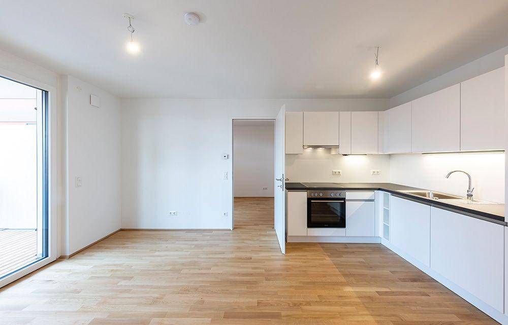 Helle Einbauküche mit weißen Schränken, dunkler Arbeitsplatte und Zugang zu einem Außenbereich.