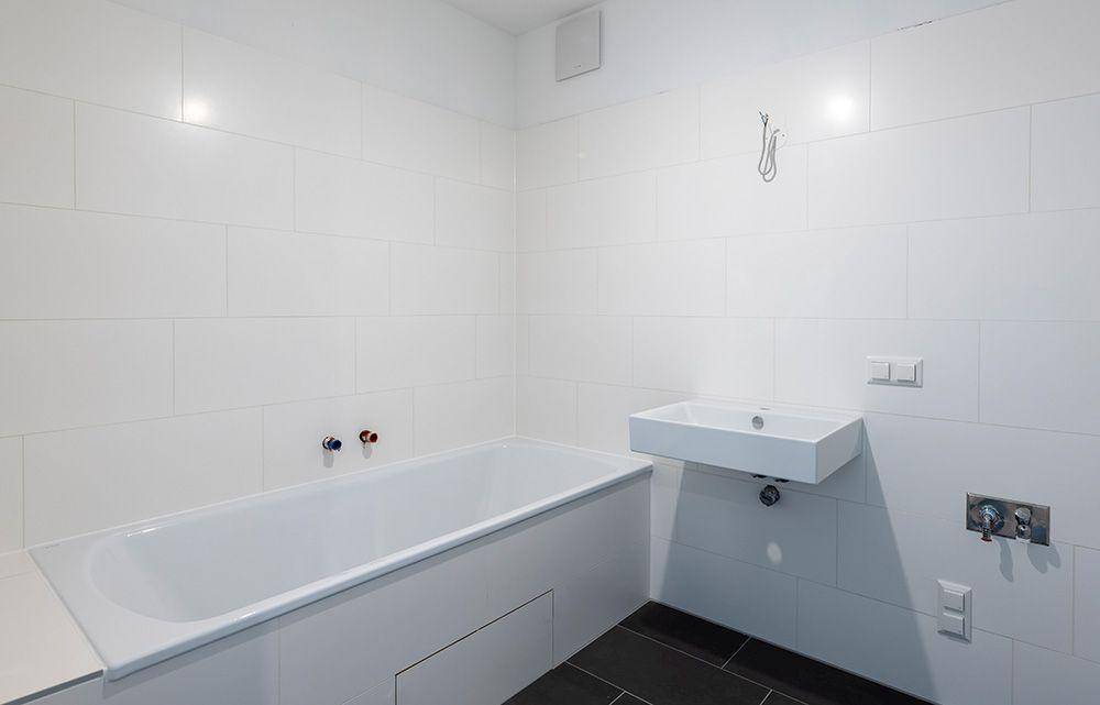 Modernes Badezimmer mit weißer Badewanne, Wandwaschbecken und dunklen Bodenfliesen.