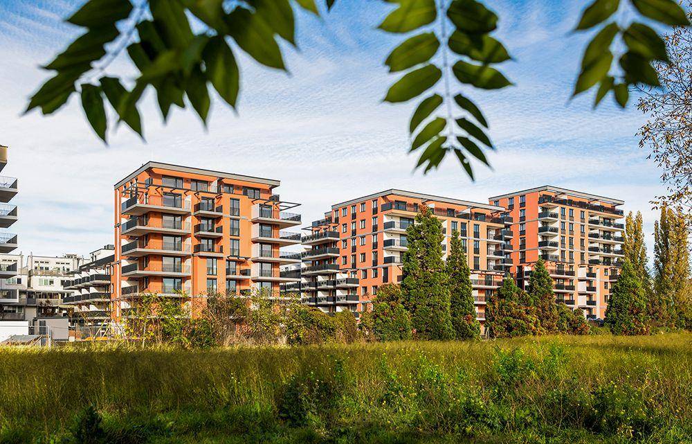 Moderne Wohngebäude mit orangefarbenen Fassaden und Balkonen, umgeben von viel Grün.