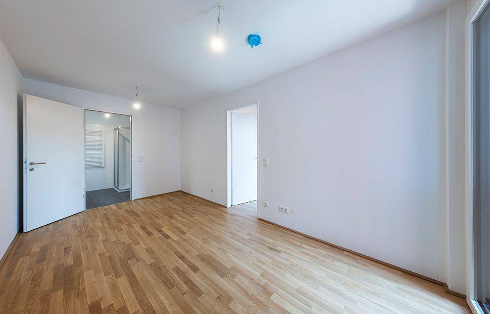 Geräumiges Schlafzimmer mit hellem Parkettboden und Zugang zu einem modernen Badezimmer mit Dusche.