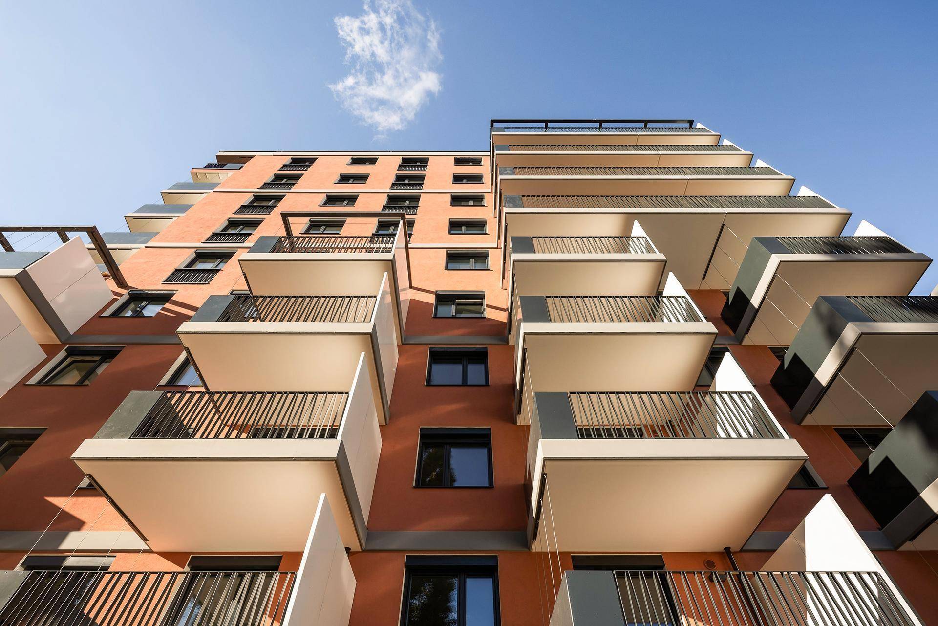 Architektonische Ansicht einer modernen Apartmentfassade mit gestaffelten Balkonen unter blauem Himmel.