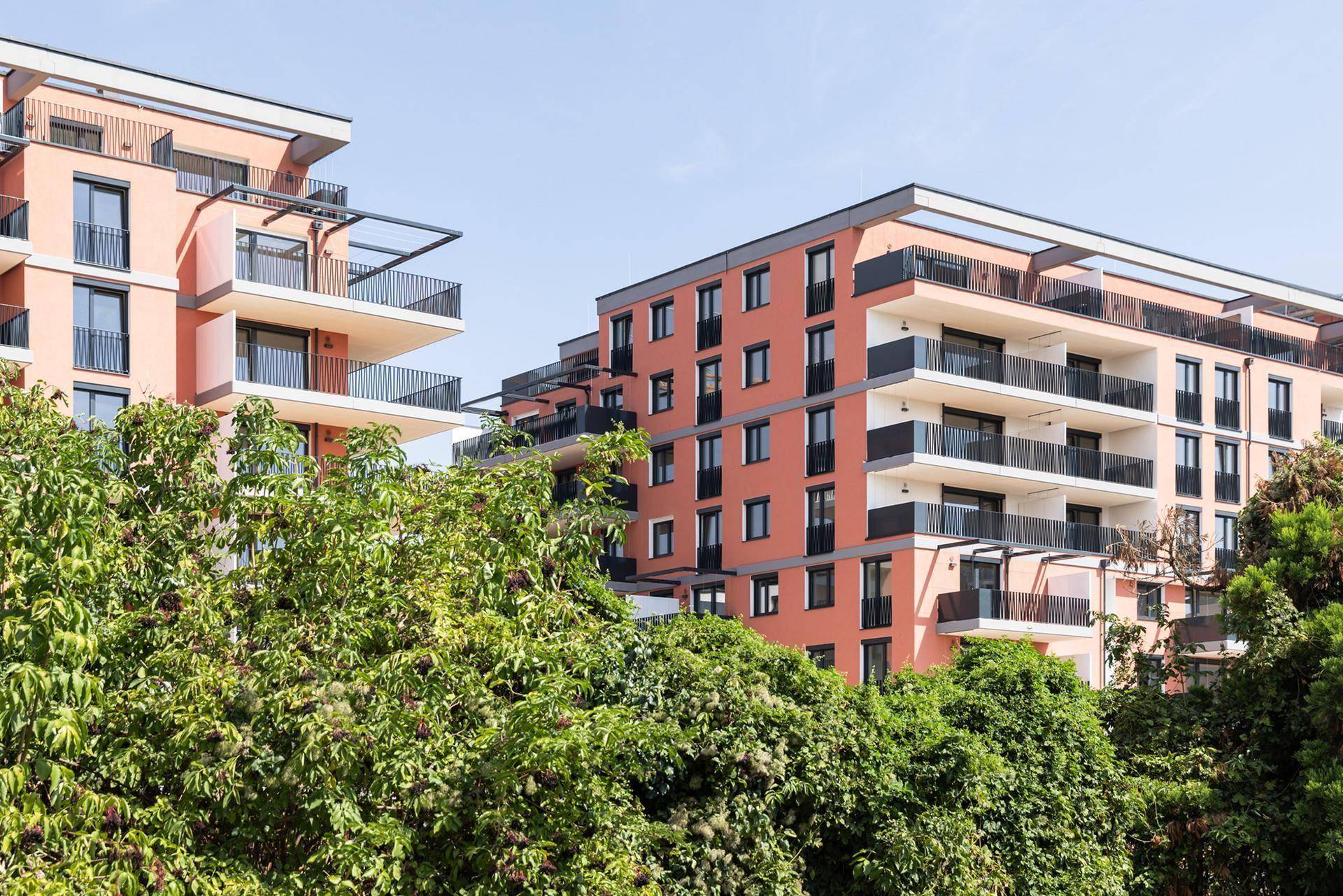 Moderne Apartmentgebäude mit Balkonen, teilweise verdeckt von dichtem grünen Laubwerk.