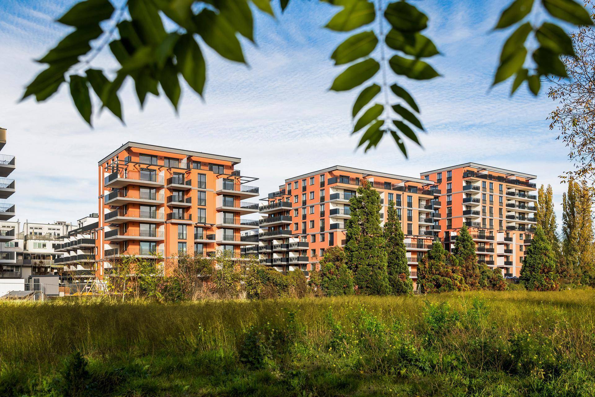 Moderne Apartmentgebäude mit Balkonen, umgeben von einer weiten grünen Wiese unter blauem Himmel.