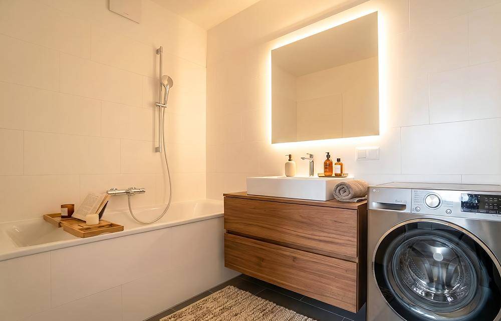 Modernes Badezimmer mit Badewanne, Waschbeckenunterschrank und integrierter Waschmaschine.