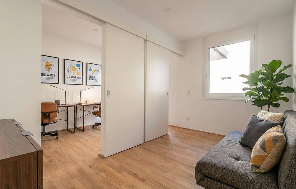 Flexibler Bürobereich mit Sofa und Schiebetüren, die zu weiteren Arbeitsplätzen führen, mit viel Tageslicht.