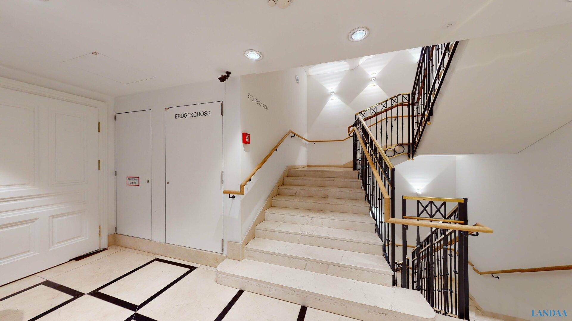 Elegantes Treppenhaus mit Marmorstufen, schmiedeeisernem Geländer und heller Beleuchtung.