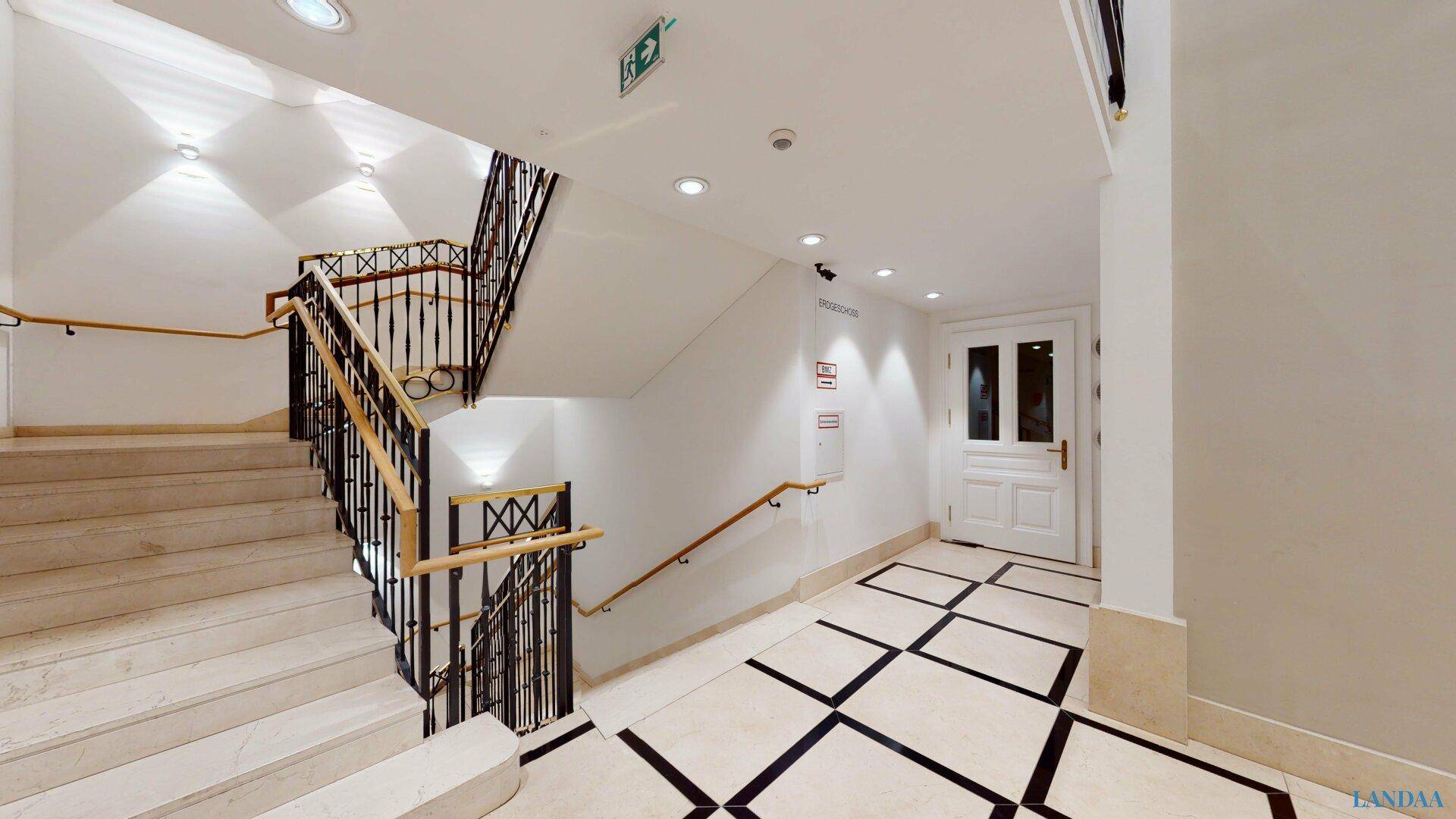 Helles Treppenhaus mit Marmorboden, klassischem Geländer und natürlichem Lichteinfall.