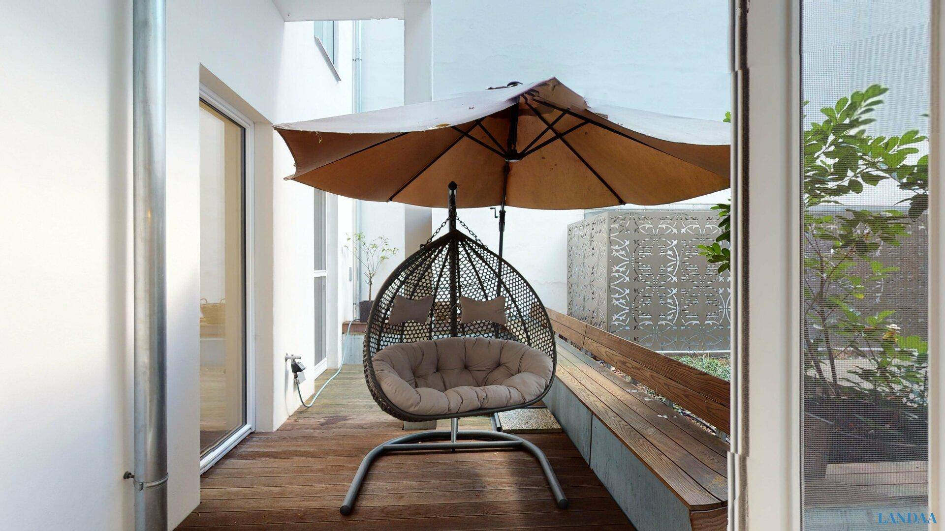 Gemütliche Terrasse mit Schaukelstuhl, Sonnenschirm und Holzboden für entspannte Stunden.