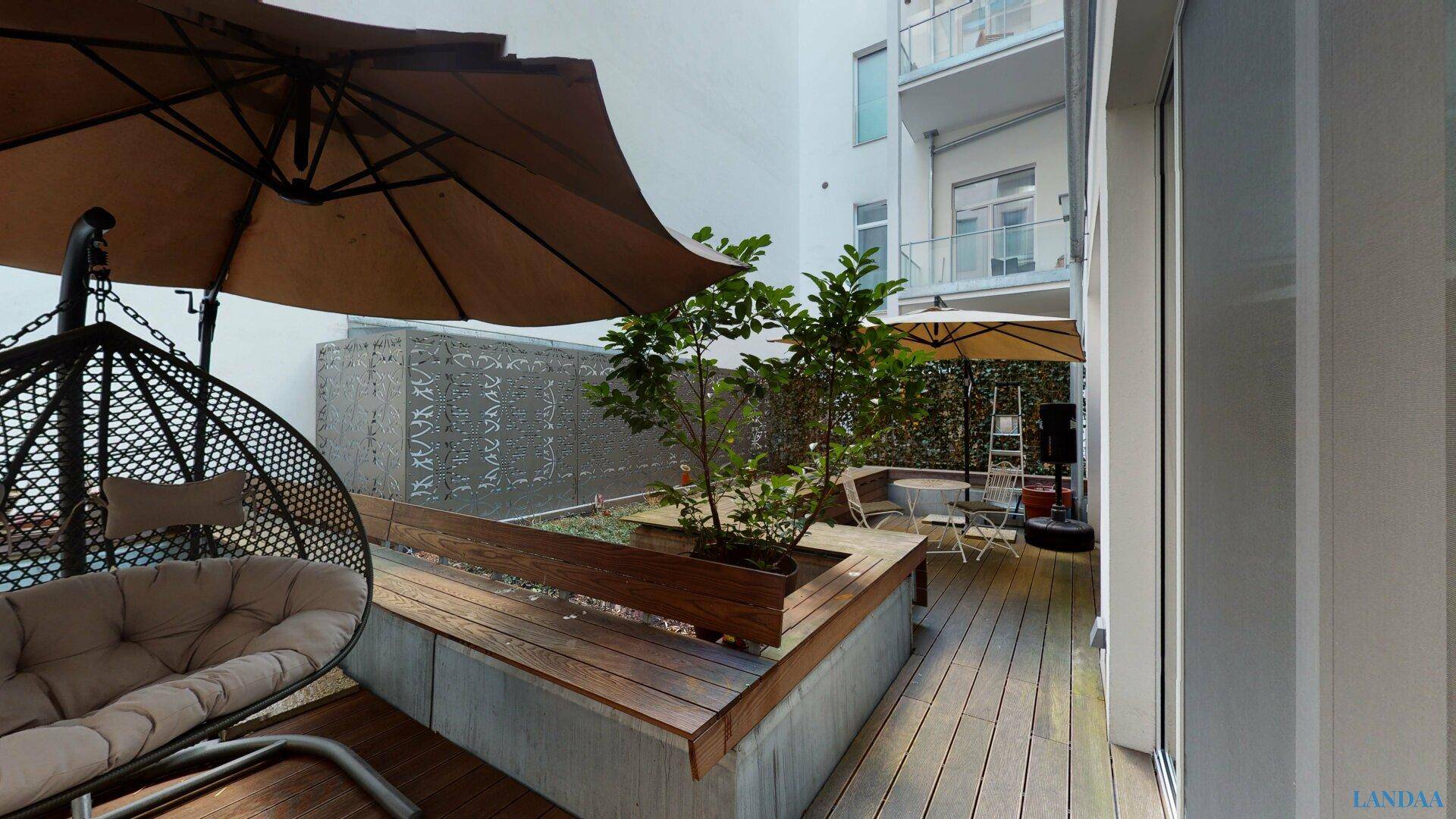 Begrünte Terrasse mit Holzdeck, Sitzgelegenheiten, Sonnenschirm und Blick auf den Innenhof.