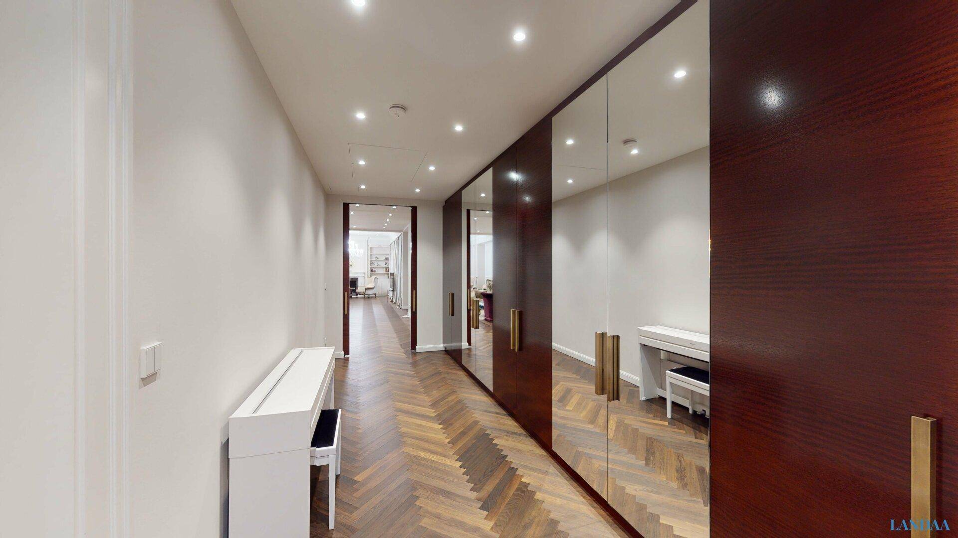 Eleganter Flur mit Fischgrätparkett, Spiegelschränken und indirekter Beleuchtung.