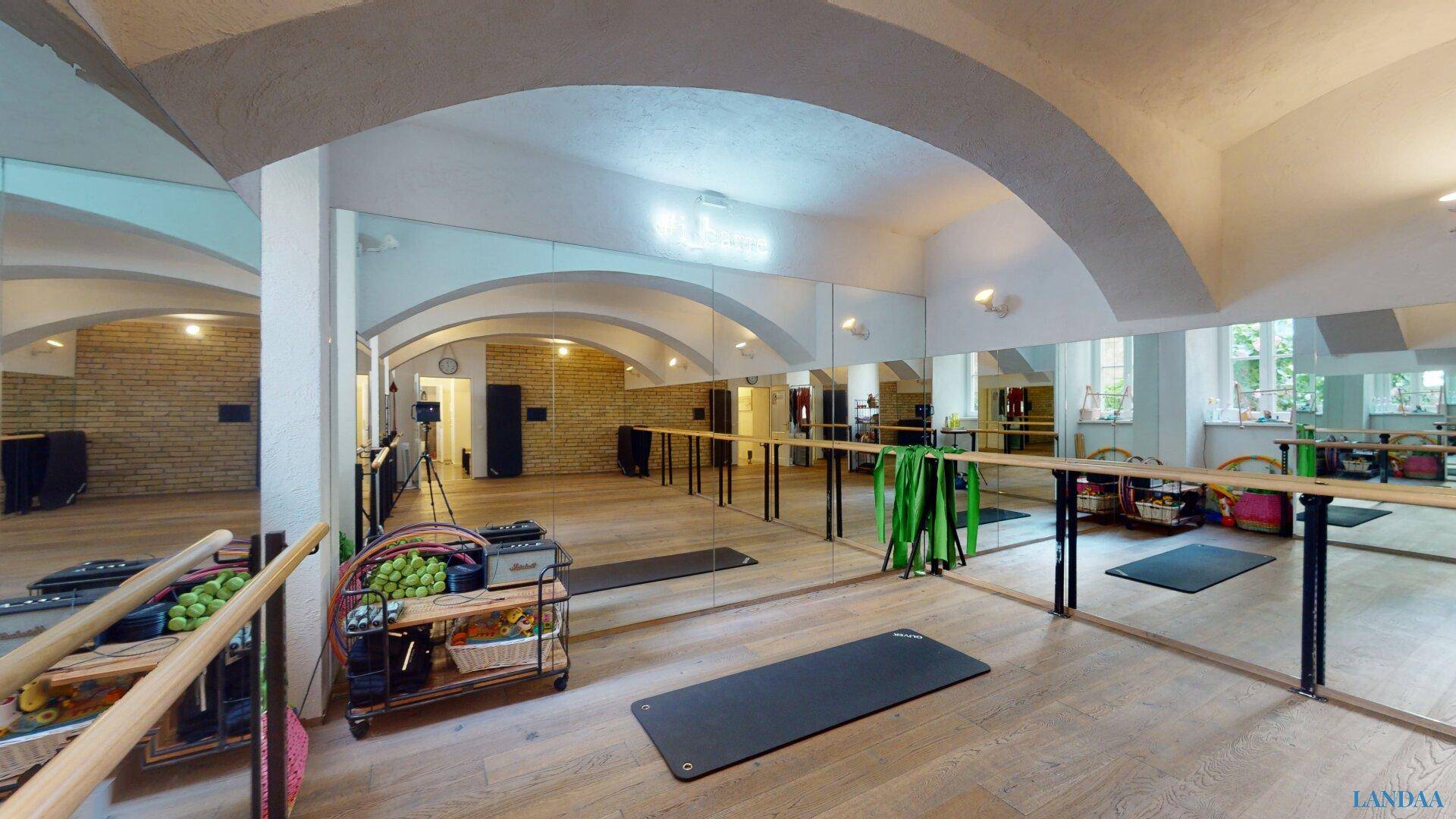 Heller Fitnessbereich mit Spiegelflächen, Holzboden und Trainingsmatten unter gewölbten Decken.