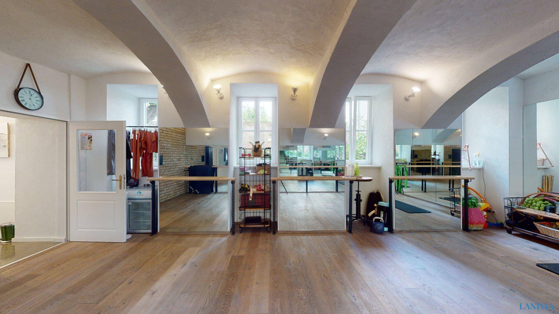Weitläufiger Trainingsraum mit hohen Fenstern, Spiegelfronten und einer einladenden Atmosphäre für Fitness.