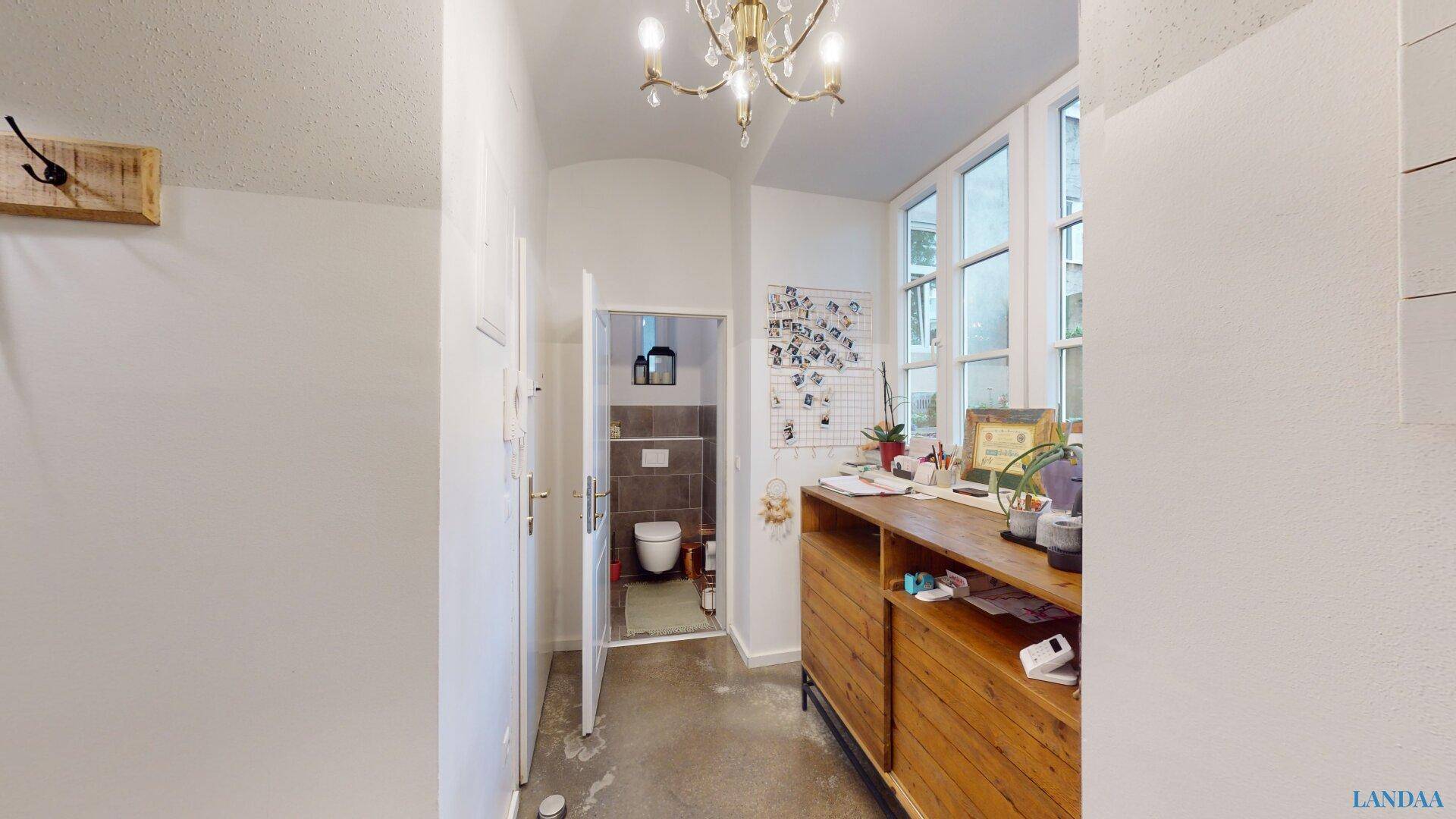 Heller Flur mit Holzkonsolentisch, Kronleuchter und Zugang zu einem separaten WC.