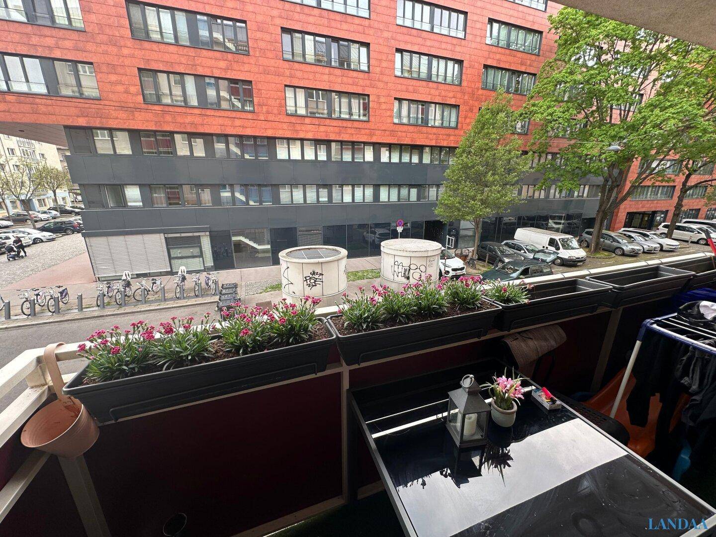 Balkon mit Blumenkästen und Blick auf die umliegenden Gebäude und die Straße.