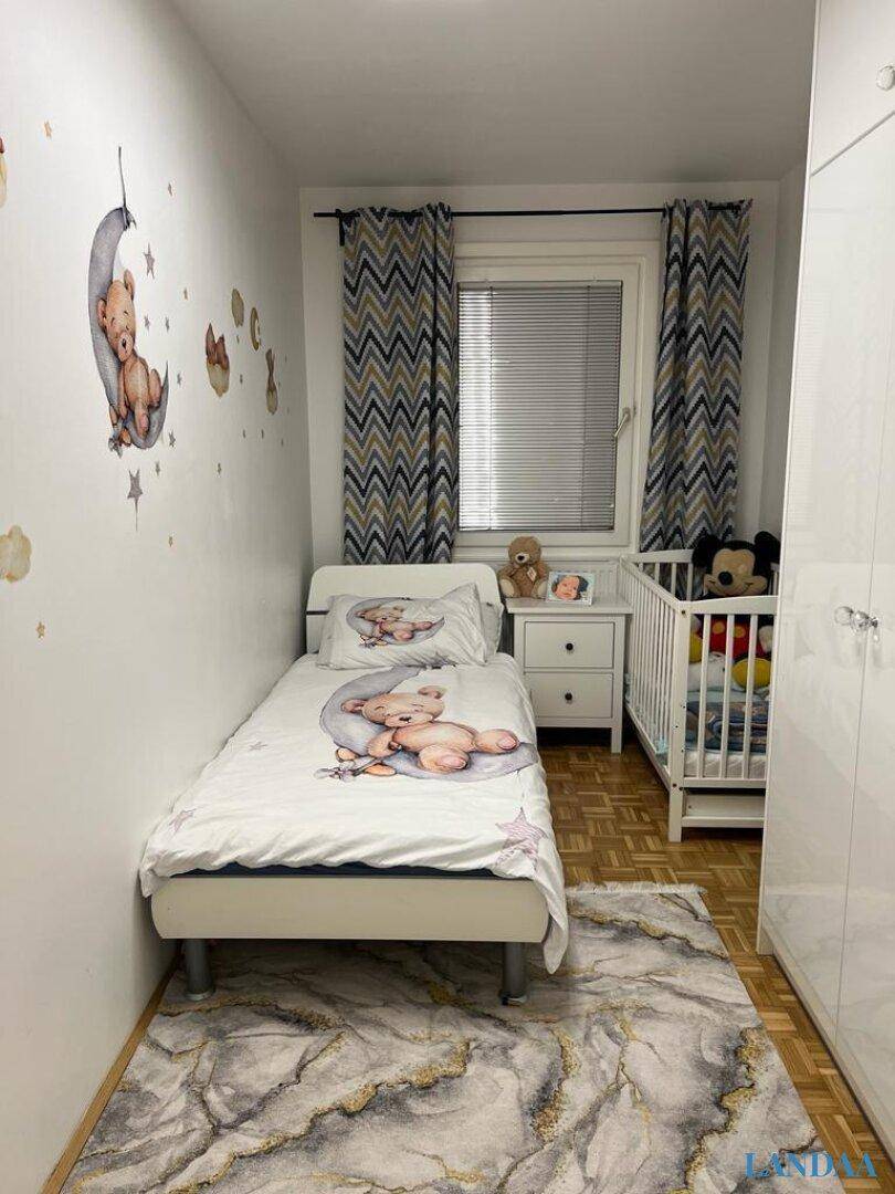 Kinderzimmer mit Einzelbett, Babybett, verspielter Wanddekoration und Fenster.