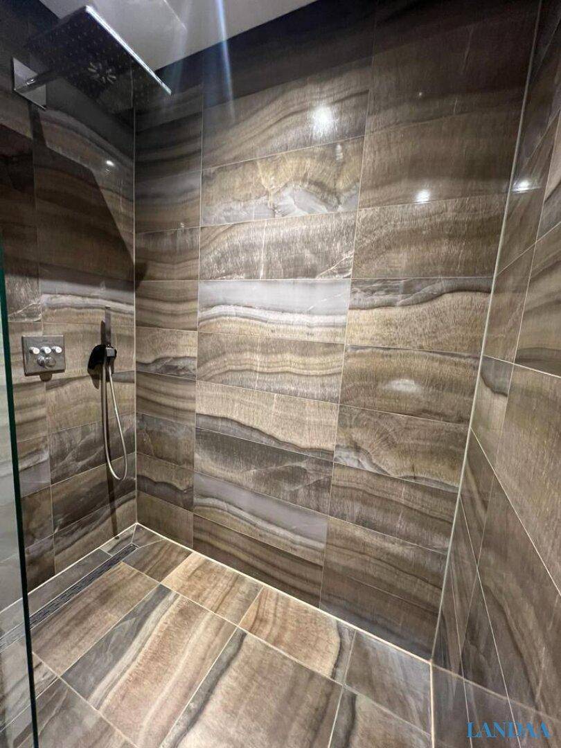 Moderne Duschkabine mit großformatigen Fliesen in Natursteinoptik und Regendusche.