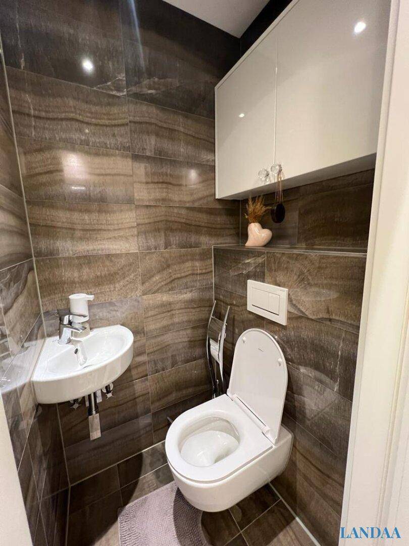 Modernes Gäste-WC mit wandhängender Toilette, kleinem Waschbecken und dunklen Fliesen.