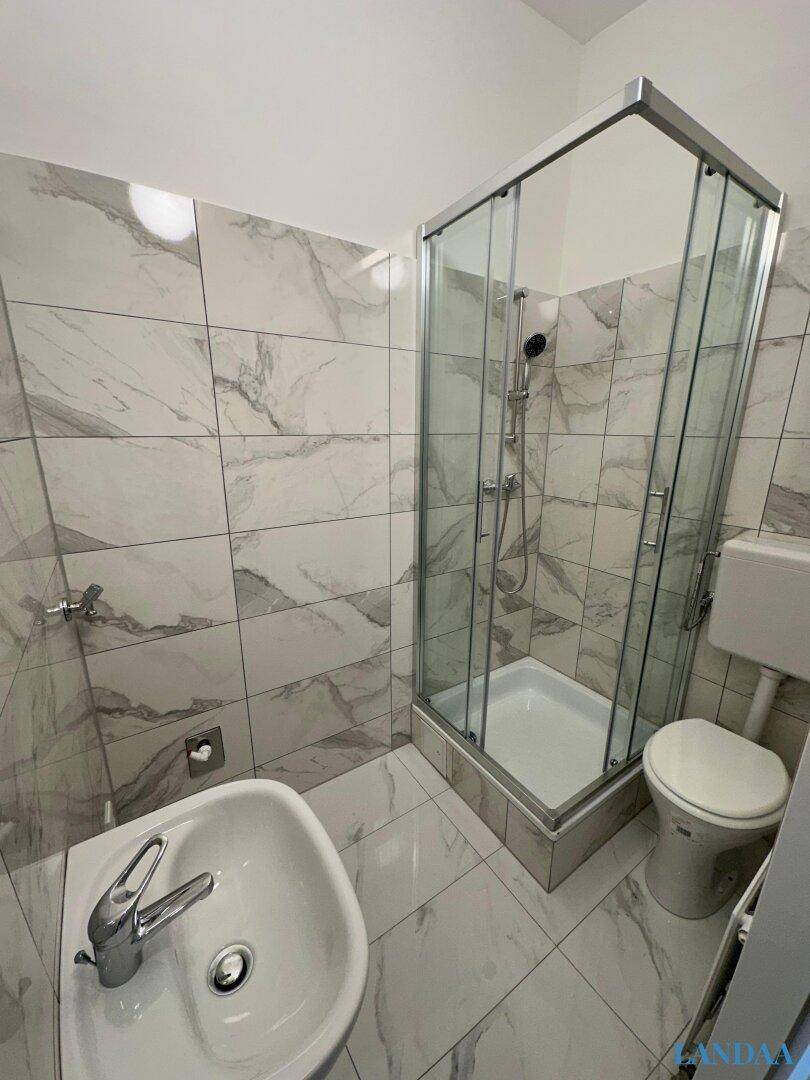 Modern gefliestes Badezimmer mit Duschkabine, WC und Waschbecken in hellen Marmoroptik-Fliesen.