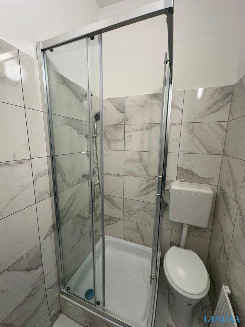Helles Badezimmer mit Duschkabine und WC, ausgestattet mit modernen, hellen Fliesen.