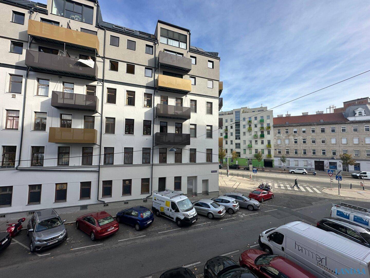 Weitläufiger Blick auf die Stadtstraße mit parkenden Fahrzeugen und angrenzenden Wohngebäuden.