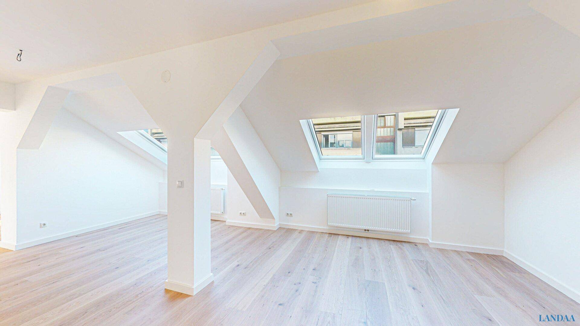 Heller, leerer Wohnraum im Dachgeschoss mit schrägen Wänden, Dachfenstern und hellem Holzboden.