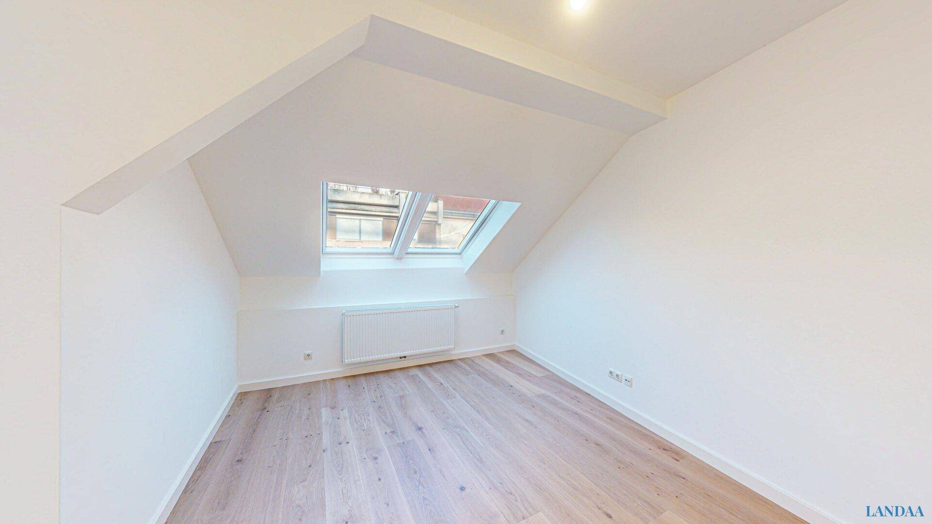 Unmöblierter Raum im Dachgeschoss mit Holzboden, Heizkörper und Dachfenster für viel Tageslicht.