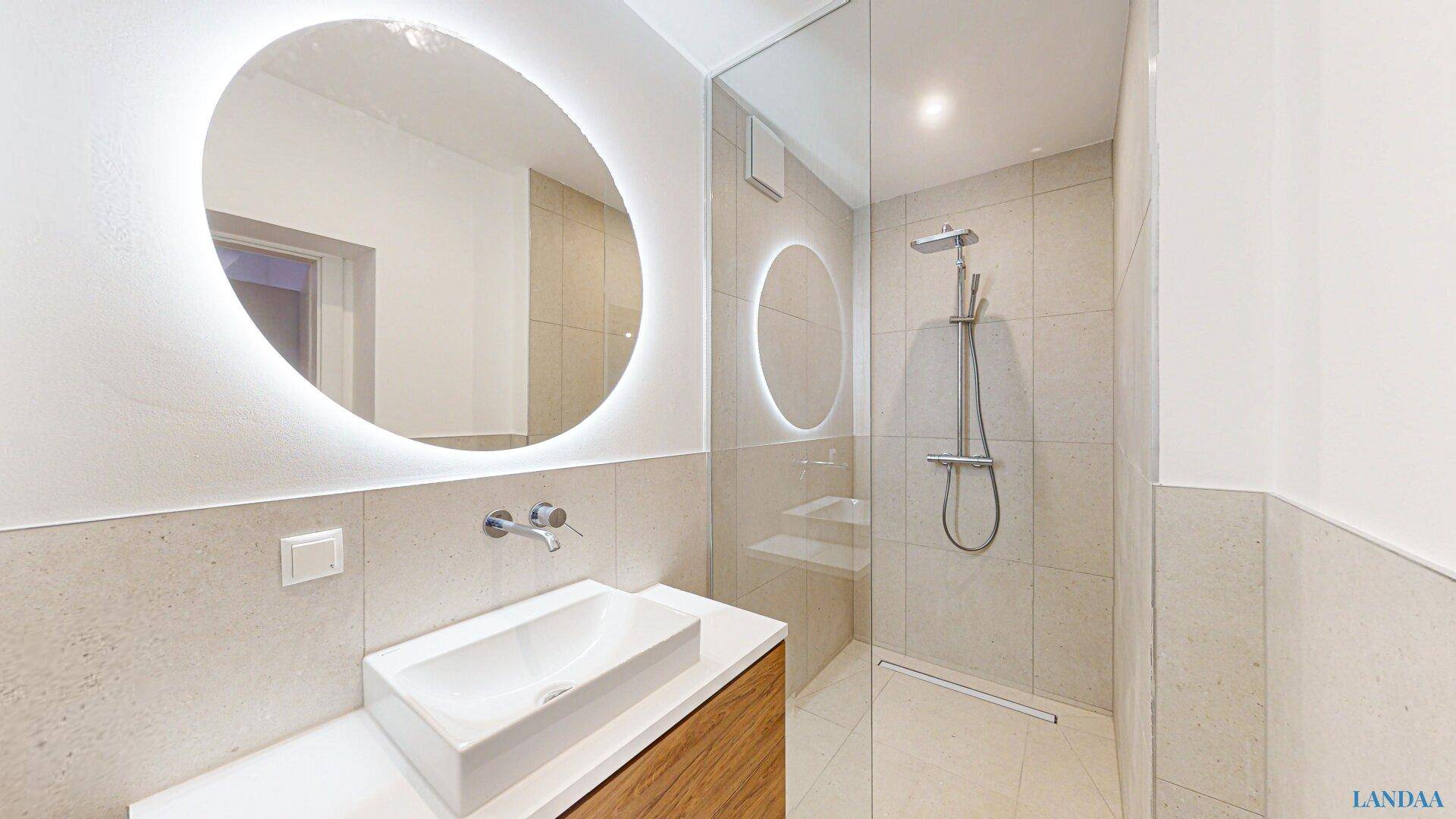 Modernes Badezimmer mit begehbarer Dusche, beleuchtetem Spiegel und eleganten Fliesen.