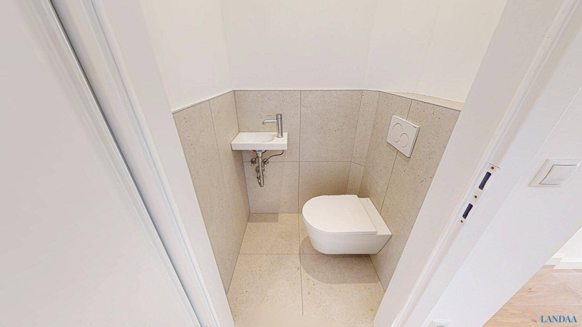 Kleines Gäste-WC mit wandhängender Toilette, kleinem Waschbecken und modernen Fliesen.