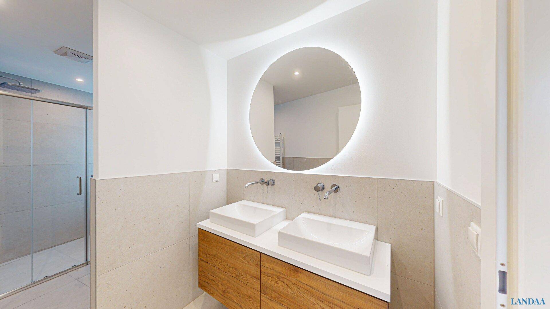 Modernes Badezimmer mit Doppelwaschbecken, beleuchtetem Spiegel und begehbarer Dusche im Hintergrund.