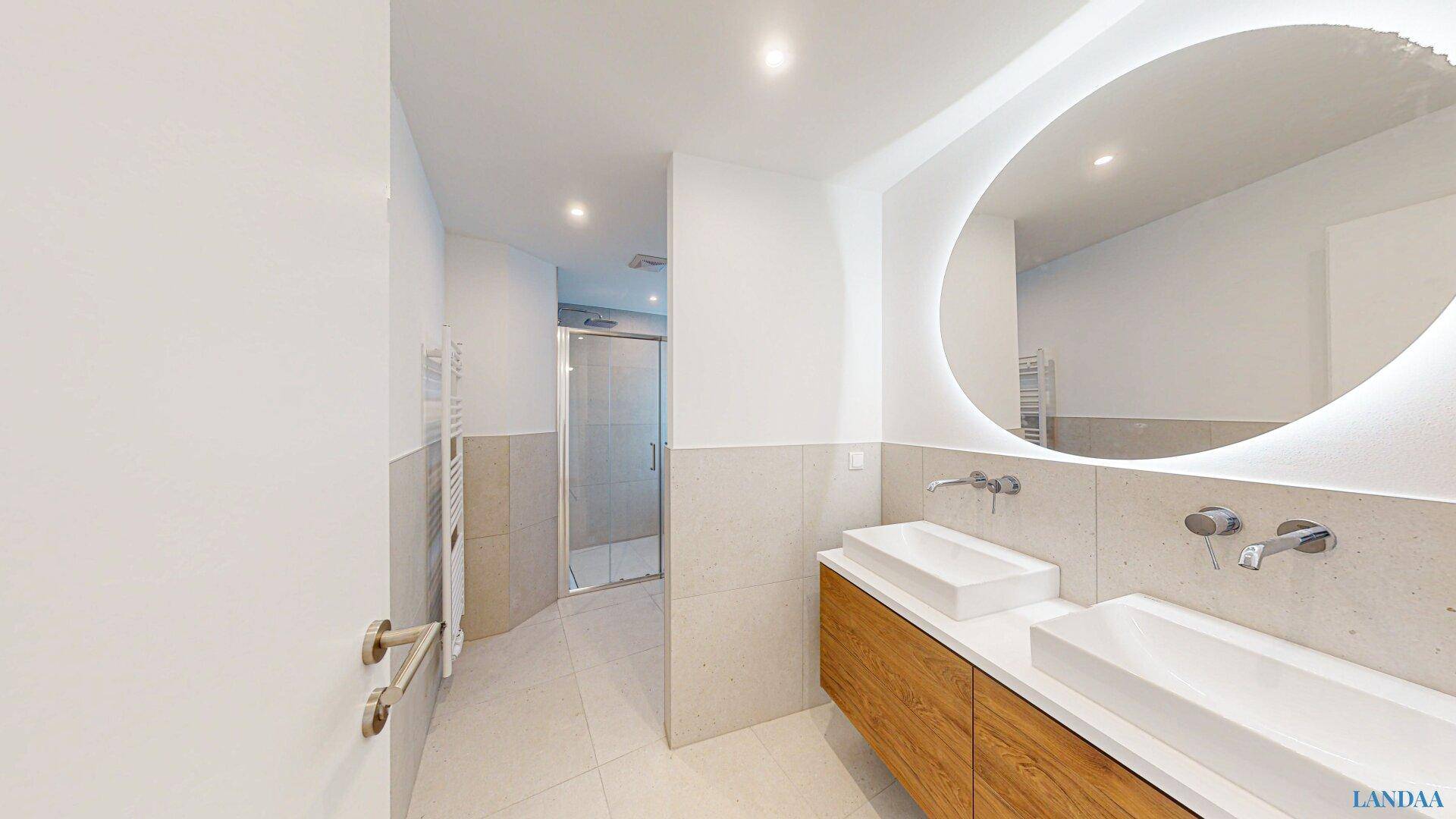 Elegantes Badezimmer mit Doppelwaschbecken, großem beleuchtetem Spiegel und Zugang zur Dusche.
