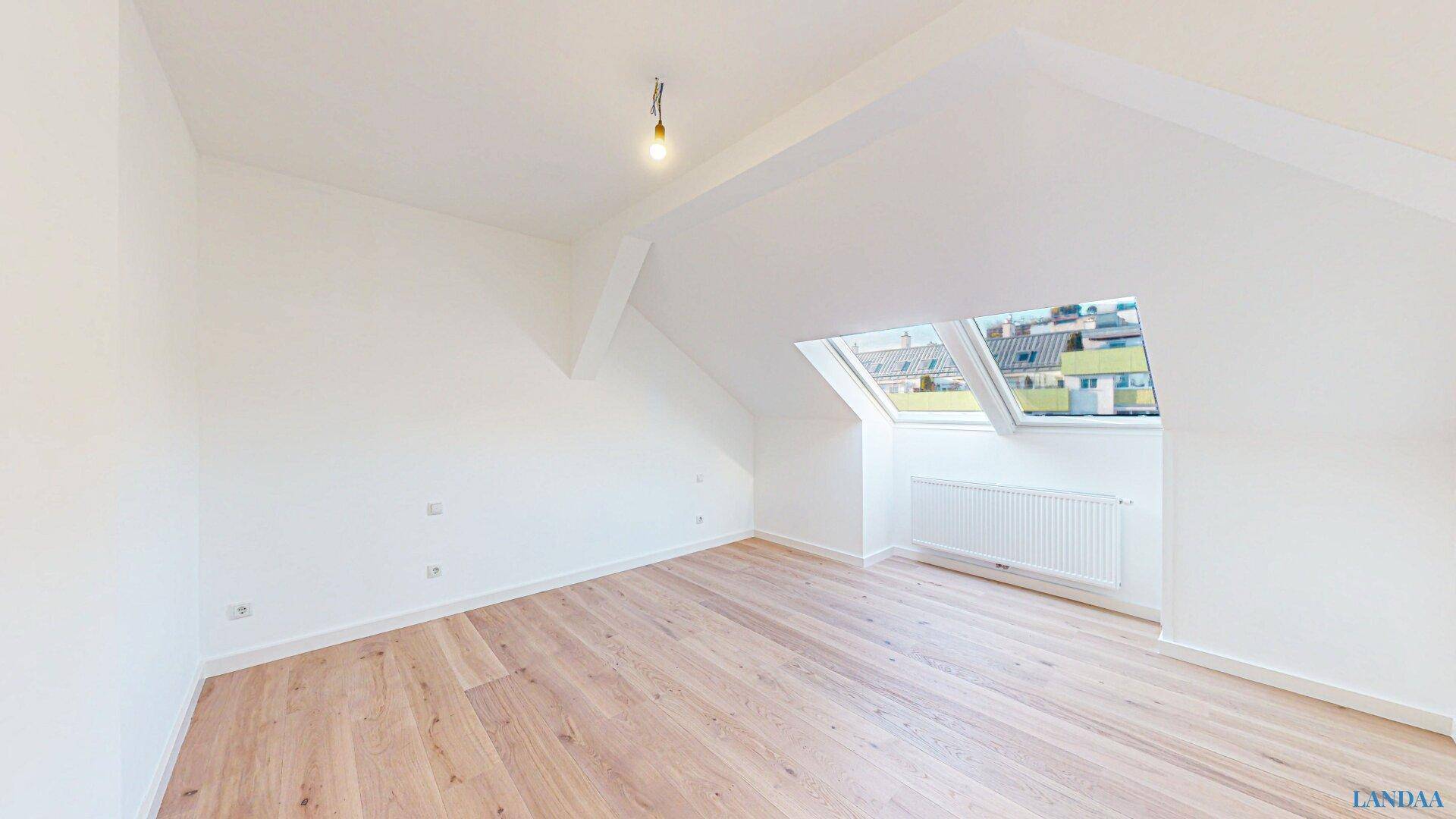 Heller, unmöblierter Raum im Dachgeschoss mit Holzboden und Dachfenstern für viel Tageslicht.