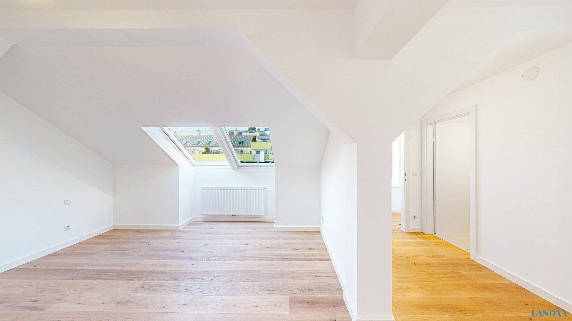 Geräumiger, leerer Raum im Dachgeschoss mit Holzboden, Dachfenster und Zugang zu weiteren Bereichen.