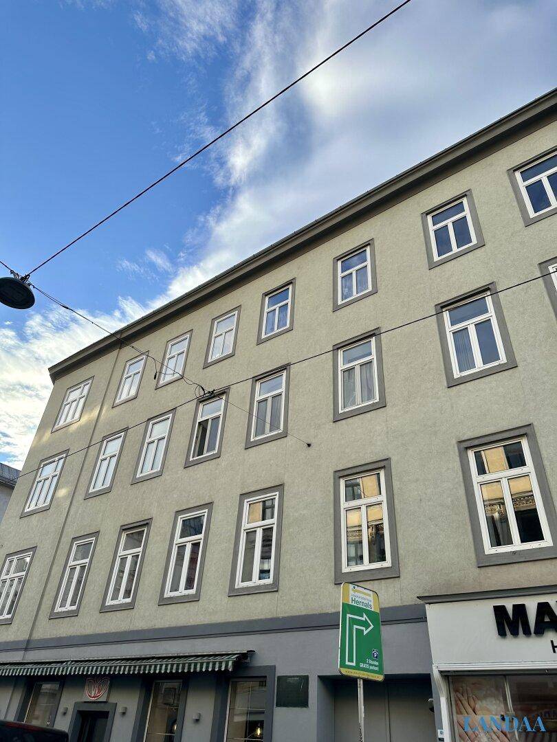 Fassade eines Altbaus mit vielen Fenstern und Geschäften im Erdgeschoss unter blauem Himmel.