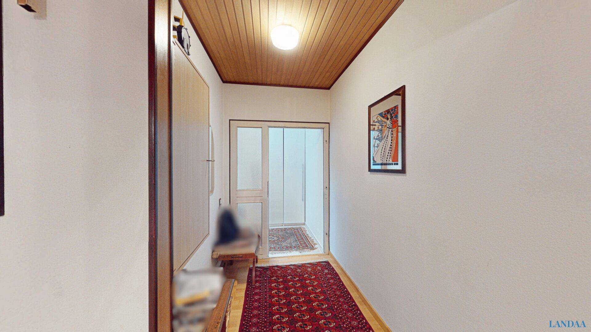 Eingangsbereich mit Holzdeckenverkleidung, Parkettboden und einem Teppich, der zur Haustür führt.