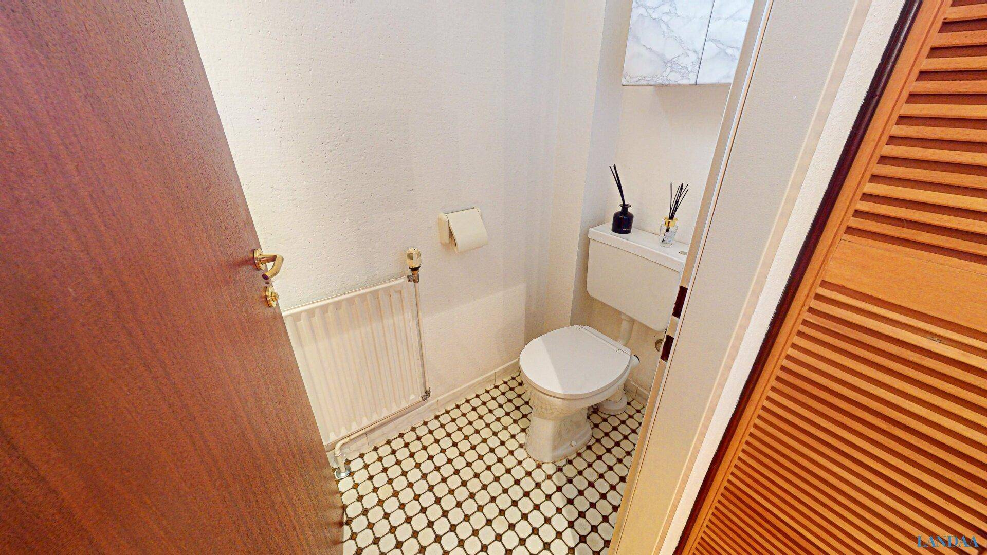 Kleines Gäste-WC mit Mosaikfliesenboden, Toilette und Heizkörper.